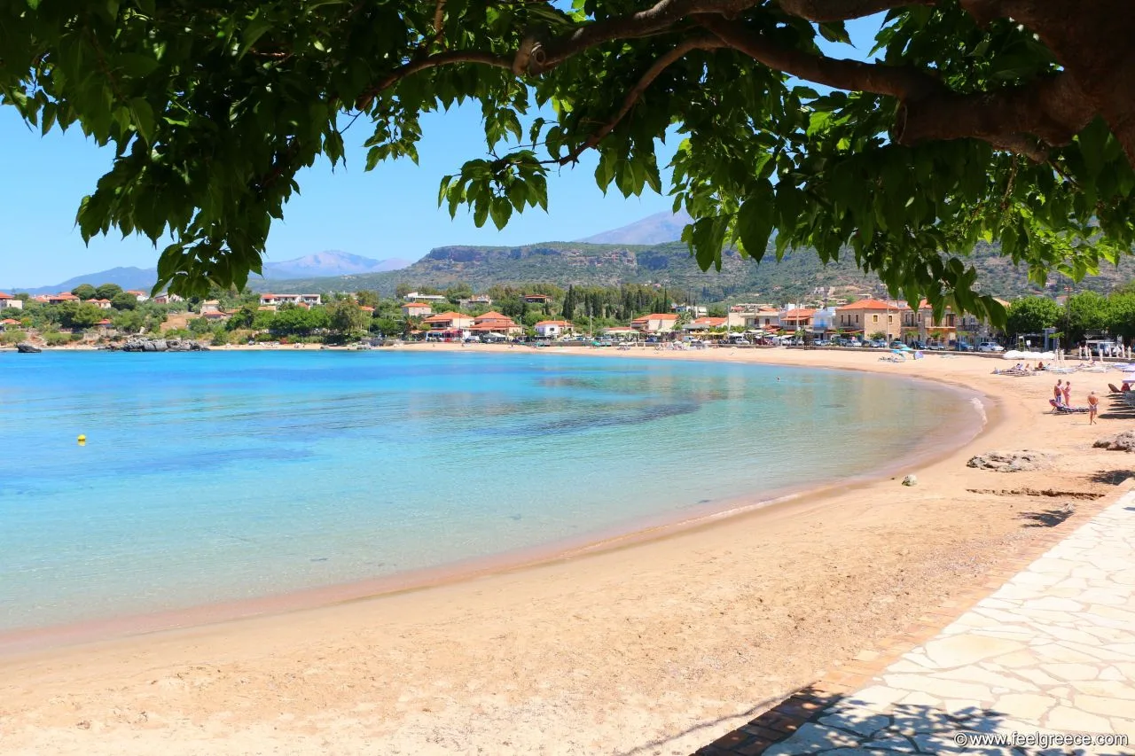 Από το δωμάτιο στη θάλασσα με σαγιονάρες: 5 μέρη στην Πελοπόννησο όπου όλα είναι δίπλα Η αμμώδης παραλία της Στούπας με γαλαζοπράσινα νερά, παραλιακά κτίρια και βουνά στο βάθος