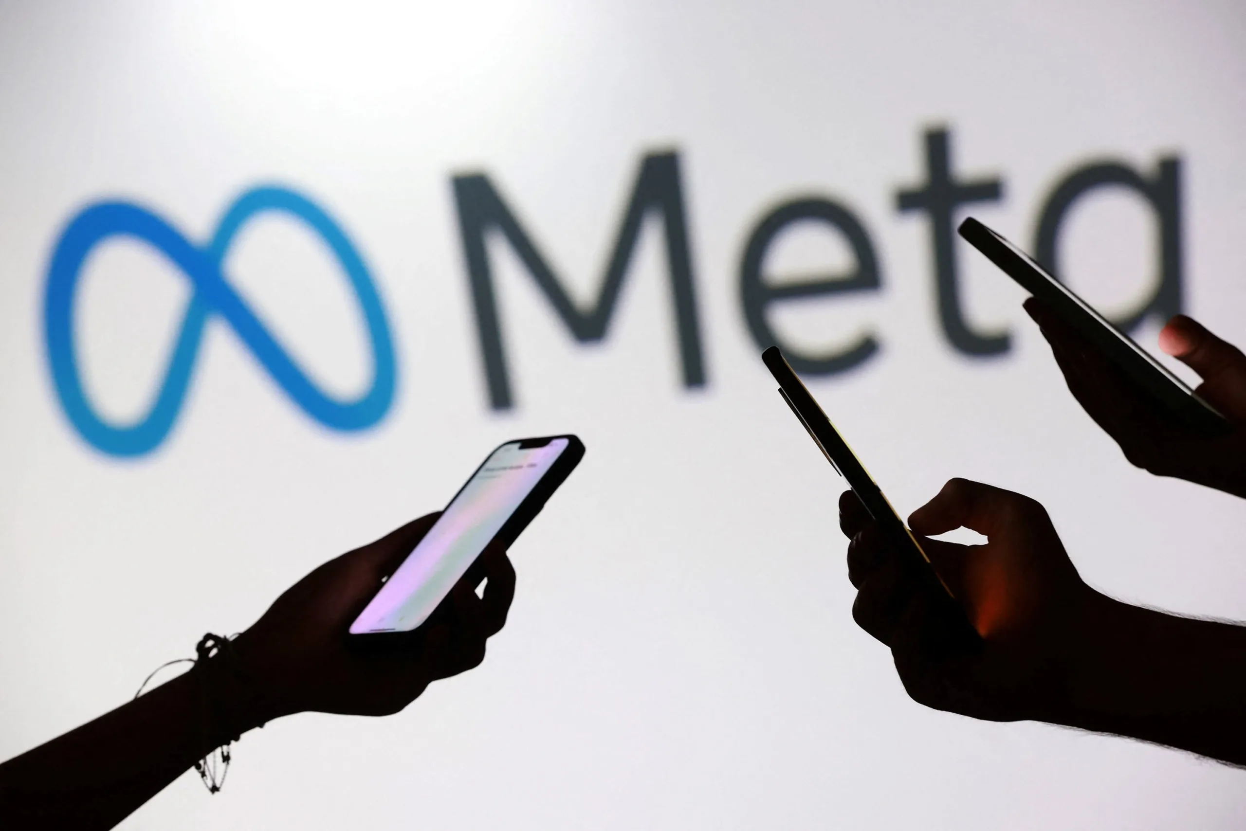 Meta: Συμβιβασμός-μαμούθ έως 16,68 δισ. δολάρια – Όρια χρήσης για τους εφήβους Σκιές ανθρώπων που χρησιμοποιούν smartphones μπροστά από το λογότυπο της Meta