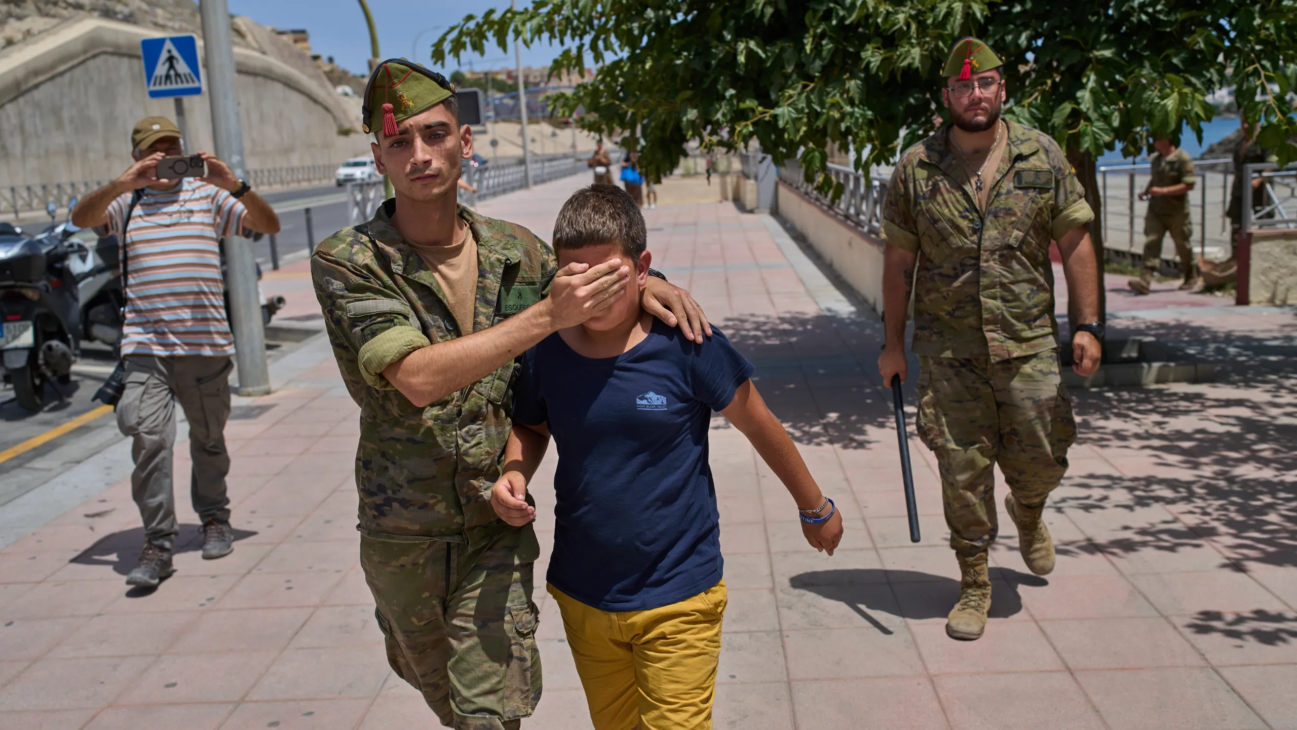 80 νεκροί και δεκάδες οικογένειες χωρίς απαντήσεις: Η δραματική επιχείρηση ταυτοποίησης στη Θέουτα Ισπανός στρατιωτικός συνοδεύει νεαρό στη Θέουτα κατά τη διαχείριση της μαζικής άφιξης μεταναστών