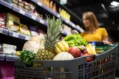 Καταναλώτρια συγκρίνει τιμές και μεγέθη συσκευασιών σε ράφι σούπερ μάρκετ