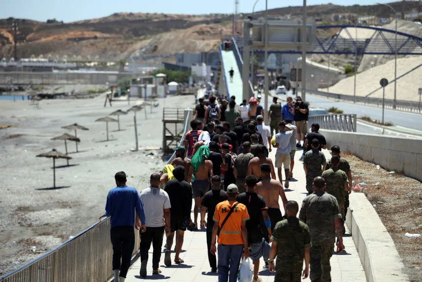 Θέουτα: 99 νεκροί και οικογένειες με φωτογραφίες στα χέρια ψάχνουν τους αγνοουμένους Ομάδα μεταναστών περπατά σε συνοριακή εγκατάσταση της Θέουτα παρουσία στρατιωτικών