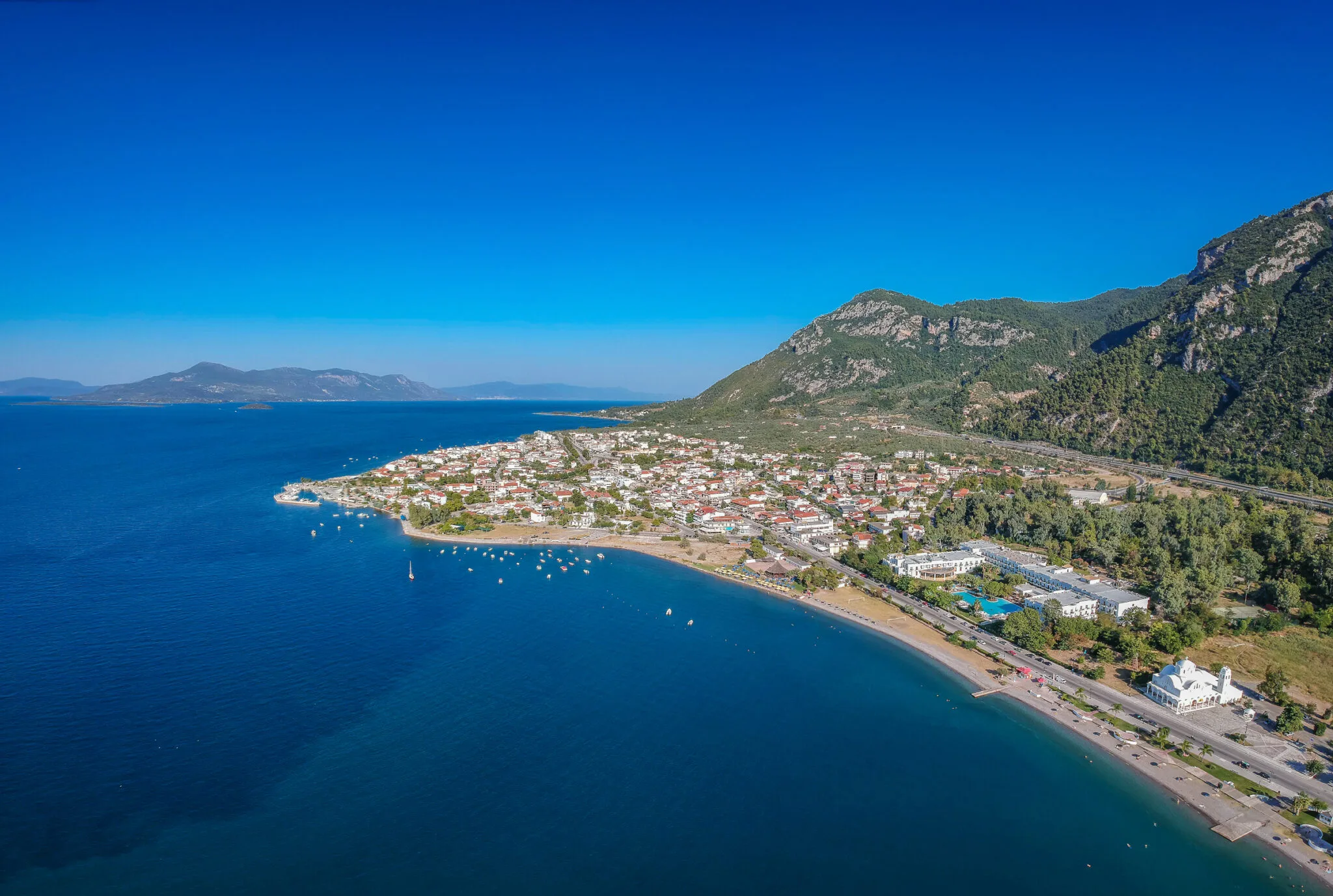 Δεν έκλεισες ακόμα διακοπές; 5 μέρη δίπλα στη θάλασσα όπου αξίζει να ψάξεις δωμάτιο τώρα Αεροφωτογραφία των Καμένων Βούρλων με τον παραθαλάσσιο οικισμό, τη θάλασσα και τα γύρω βουνά