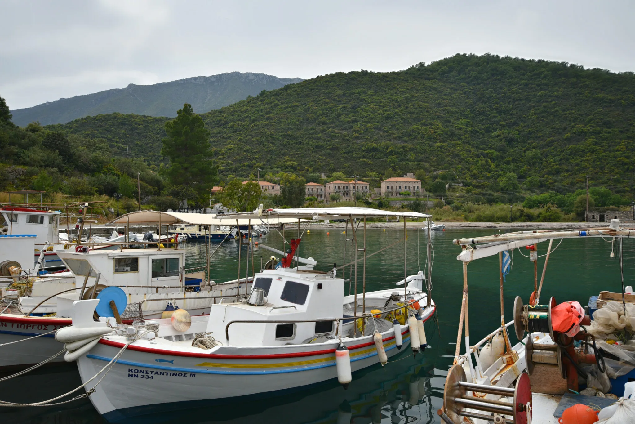 Χωρίς πλοίο, μακριά από τα συνηθισμένα: 6 στάσεις από το Λεωνίδιο στη Μονεμβασιά Ψαρόβαρκες δεμένες στο μικρό λιμάνι των Πουλίθρων με πέτρινα σπίτια και καταπράσινους λόφους στο βάθος