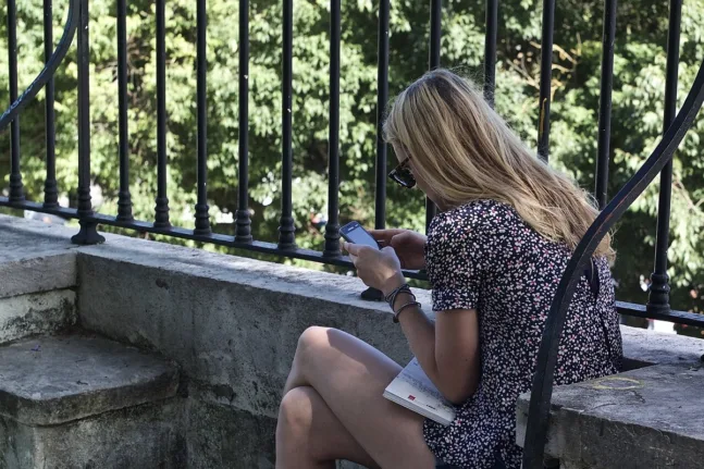 Αναγνώστρια κοιτάζει το smartphone ενώ κρατά βιβλίο