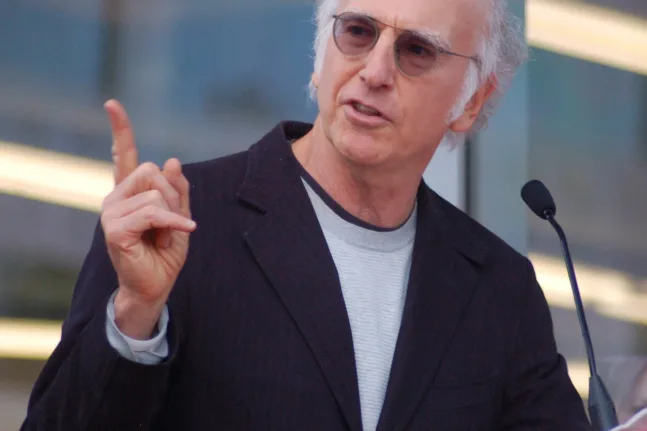 Ο Larry David μιλά σε μικρόφωνο και υψώνει το χέρι του.