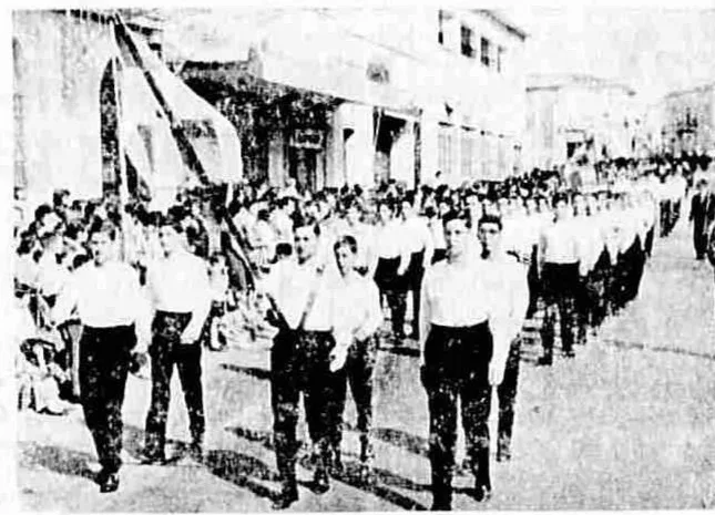 28η Οκτωβρίου στην Πάτρα: Όταν το ’40 καθόταν απέναντι από την εξέδρα Μαθητές παρελαύνουν με τη σημαία, μπροστά από τα παλιά κτίρια και τους θεατές στην Πάτρα.