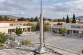 Συμβολική εικόνα αλεξικέραυνου σε στέγη, με σχολικά κτίρια στο βάθος.